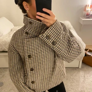 Rutig kappa med hög krage - Säljer en snygg rutig kappa från Pernilla Wahlgrens märke som är jättelik den från ARKET. Mönstret är i svart, brun och Cremevit. Den är tyvärr för stor för mig som är 150cm har inte råd att lämna in till skräddare så därför måste jag sälja den🥲Man kan ha kragen uppe eller ha den nere (bild 2) jättefint skick inga lösa trådar eller andra defekter😁Kan tänka mig gå ner i pris vid snabb affär