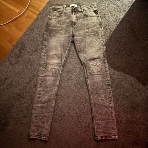 Grå slitna jeans från Replay - Grå jeans från Replay i slim tapered fit med snygga slitningar och tvättad look. Klassisk femficksmodell, smal passform som smalnar av vid ankeln. Perfekta för dig som gillar en edgy stil och vill ha jeans med attityd. 😎