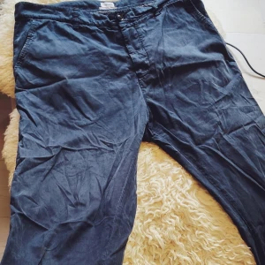 Mörkblå Filippa K Chinos stl 50 - Snygga mörkblå manchesterbyxor från Filippa K i storlek 50. Byxorna har klassisk rak passform med sidfickor och knappgylf. Perfekta för dig som gillar stilrena och bekväma byxor med lite retrovibe.