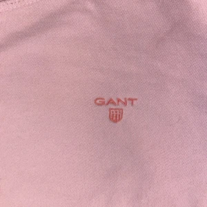 Ljusrosa sweatshirt från GANT - Säljer en stilren ljusrosa sweatshirt från GANT med broderad logga på bröstet. Tröjan har rund halsringning, långa ärmar och är tillverkad i mjuk bomull. Perfekt för dig som gillar klassisk och enkel stil.