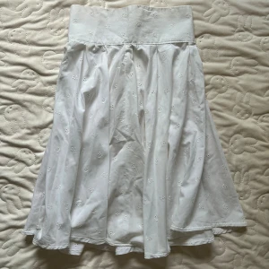 Vit långkjol med broderade detaljer (S/M) - Säljer en vit långkjol med bred linning och små broderade blommor över hela kjolen. Kjolen har knappar och dragkedja i sidan för enkel påklädning. Materialet är mjukt och känns som bomull, perfekt för dig som gillar romantiska och söta plagg.