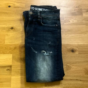 Hoodrich Jeans - Snygga mörkblå skinny jeans från Hydeorigin med slitna detaljer och ljusa partier på låren. Klassisk femficksmodell med broderad logga på bakfickan och text på insidan av linningen. Perfekta för en trendig streetstil.