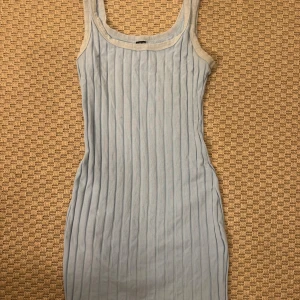 Ljusblå ribbad ärmlös klänning - Säljer en ljusblå ribbad klänning med smal passform och ärmlös design. Klänningen har en rundad halsringning och vertikala ribbade ränder som ger en snygg struktur. Perfekt för dig som gillar enkel och stilren look.