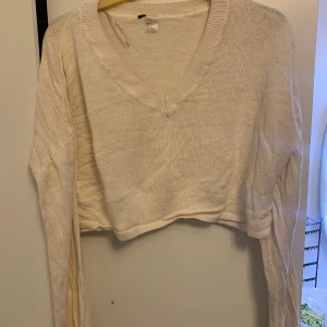 Vit croppad stickad tröja H&M - Säljer en vit croppad stickad tröja från H&M med v-ringning och långa ärmar. Tröjan har en ribbad kant vid halsen och är perfekt för lager-på-lager. Enkel och stilren design som passar till allt.