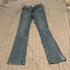 Blå jeans med slits nertill - Säljer ett par klassiska blå stretchjeans med raka ben och snygg slits nertill på utsidan av benen. Jeansen har fem fickor och normal passform, perfekta för en chill och trendig look. Materialet är robust denim som håller länge.