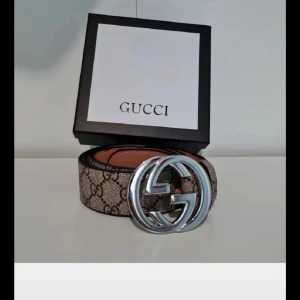  GG Supreme bälte med silverdetalj - Säljer ett  GG Supreme bälte i beige och brunt med klassiskt monogrammönster och stor silverfärgad GG-spänne. Bältet är gjort i exklusivt skinn och kommer med originalbox, kvitto och kontrollkort. Perfekt accessoar för att lyfta din outfit.