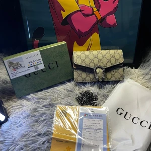 Supreme axelväska - Snygg  Dionysus axelväska i beige  Supreme canvas med klassiskt monogrammönster och silverfärgad kedja. Väskan har ett dekorativt spänne framtill och detaljer i skinn. Perfekt för dig som vill ha en ikonisk och trendig accessoar.