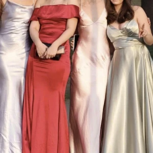 Ljusrosa balklänning med slits - Supersnygg ljusrosa långklänning i satinliknande material med smala axelband, v-ringning och slits framtill. Klänningen har en elegant och minimalistisk design som ger en lyxig känsla. Perfekt för dig som vill sticka ut med en stilren look.