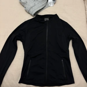 Svart zip jacka från Aim'n - Svart zip jacka från Aim'n med lång ärm, hel dragkedja framtill och två fickor med dragkedja. Jackan är figursydd och har tumhål vid ärmsluten. Tunt och skönt material att träna i🫶🏽