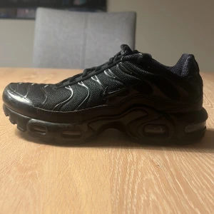 Nike Air Max Plus helsvarta sneakers - Säljer ett par helsvarta Nike Air Max Plus sneakers med mesh- och syntetöverdel, ikoniska vågiga detaljer och synlig Air-dämpning i sulan. Skorna har snörning och en chunky, sportig vibe som sticker ut. Perfekta för dig som gillar streetstyle och komfort.