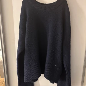 Mörkblå stickad tröja Gina Tricot - Mysig mörkblå stickad tröja från Gina Tricot med rund hals och långa ärmar. Tröjan har en loose passform och breda ribbade muddar vid hals, ärmslut och nederkant. Perfekt för kyliga dagar och enkel att matcha med jeans eller kjol.