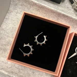 Silvriga örhängen med nitar - Coola silvriga örhängen i form av små hoops med spetsiga nitar runt om. Ifrån Edblad och kommer med box.
