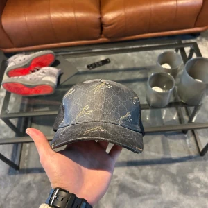 Gucci keps - Snygg svart keps från Gucci med klassiskt GG-monogram och broderade tigrar i guld. Kepsen har mesh på sidorna och justerbar rem bak. Tillverkad i bomull och polyester, perfekt för dig som vill sticka ut med en exklusiv accessoar.