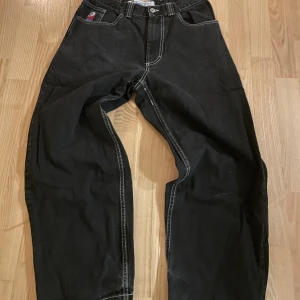 Svarta Big Boy jeans med brodyr - Svarta jeans från Big Boy med kontrasterande vita sömmar och en broderad figur på myntfickan. Jeansen har en loose passform och raka ben, klassisk femficksdesign och tydlig streetwear-vibe. Perfekta för dig som gillar baggy stil.