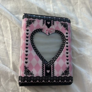 Söt rosa och svart Photo Cards hållare - Photo  card hållare i rosa och svart med harlekinrutor, hjärtmönster och spetsdetaljer. Framsidan har ett stort hjärta med svart spetskant och en rosa rosett. Insidan har plastfickor för kort eller foton. Perfekt accessoar för dig som gillar gulliga detaljer. Däremot har jag klippt lite i slutet inget man tänker på men det är bra att veta