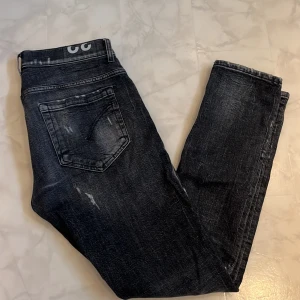 Svarta skinny jeans från Dondup - Säljer ett par svarta skinny jeans från Dondup, modell George. Jeansen har slitna detaljer och en tvättad look med fem fickor och knappstängning. Materialet är bomull med lite stretch för skön passform. Perfekt för dig som gillar en edgy stil.