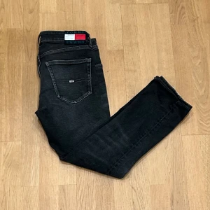 Svarta Tommy Jeans Scanton Slim W30 L34 - Svarta slim fit jeans från Tommy Jeans, modell Scanton. Klassisk femficksdesign, diskret logga på bakfickan och tydlig Tommy Jeans-etikett i midjan. Jeansen har en smal passform och är tillverkade i stretchig denim för extra komfort. Storleken är 30/34 men har sytt upp de till 30/32