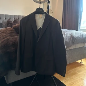 Svart kavaj från Oscar Jacobson - Stilren svart kavaj från Oscar Jacobson, modell Sartorial Leisure. Klassisk passform med två fickor framtill och knappar vid ärmslut. Perfekt för dig som vill ha en tidlös och snygg look. Fodrad insida med diskret mönster.