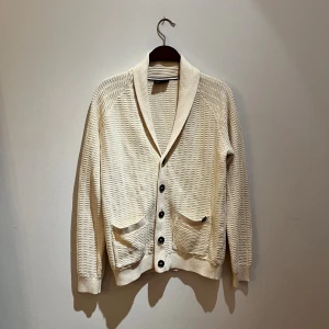 Beige kofta från Lindbergh, M - Säljer en beige kofta från Lindbergh i stickad bomull. Koftan har snygg struktur, två framfickor och stängs med svarta knappar. Perfekt för lager-på-lager och har en klassisk krage som ger en clean look. Hör av er vid frågor och priset är inte hugget i sten