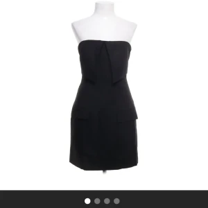 Svart axelbandslös klänning Adoore - Svart axelbandslös kortklänning från Adoore med snygg detalj framtill och dragkedja i ryggen.         Säljer då den ej kommer till användning, aldrig använd endast testat! Alla lappar sitter kvar