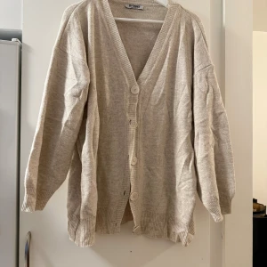 Beige kofta från My Fashion - Beige kofta från My Fashion med v-ringning och stora knappar framtill. Koftan har ribbade muddar och är långärmad med en loose passform. Perfekt för lager-på-lager och chill dagar.