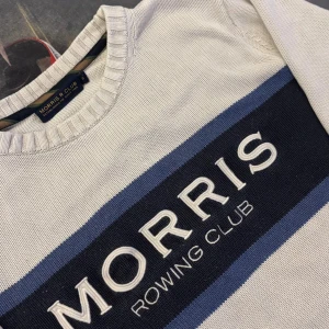 Stickad Morris Rowing Club tröja - Vit stickad tröja från Morris Rowing Club med blå och marinblå ränder över bröstet och broderad logga. Rund halsringning och ribbade muddar vid ärmslut och nederkant. Perfekt för en stilren look.
