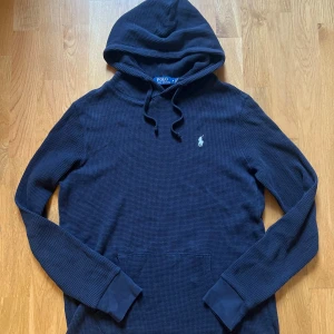 Mörkblå stickad hoodie från Polo Ralph Lauren - Säljer en mörkblå hoodie från Polo Ralph Lauren med klassisk broderad logga på bröstet. Tröjan har huva med snörning och en waffle struktur| skriv vid minsta fundering priset kan såklart diskuteras !