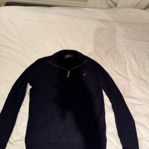 Mörkblå merinoullströja Morris S - Säljer en mörkblå kabelstickad tröja från Morris i 100% merinoull. Tröjan har lång ärm, ribbade muddar och en snygg half zip-dragkedja vid halsen. Perfekt för dig som gillar klassisk och stilren look.