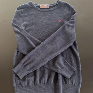 Mörkblå merinoullströja från Morris - Snygg mörkblå stickad tröja från Morris i 100% merinoull. Klassisk rund halsringning och diskret röd broderad logga på bröstet. Perfekt för dig som gillar stilrena och bekväma plagg med premiumkänsla.