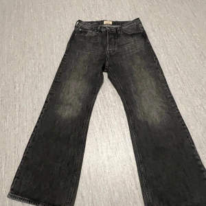 Svarta wide jeans från Jack & Jones - Säljer ett par svarta jeans från Jack & Jones med snygg tvättad look. Modellen har breda ben och klassisk femficksdesign. Jeansen är tillverkade i denim och har en läderpatch med logga bak i midjan. Perfekta för dig som gillar en avslappnad och trendig stil.