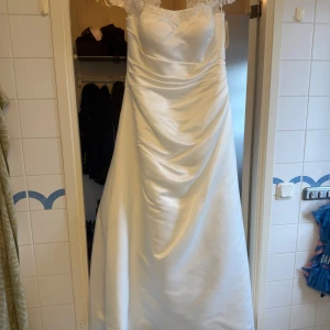 Brudklänning Ivory långklänning Gaby med spets - Elegant långklänning i ivory med vackra spetsdetaljer vid axlar och halsringning. Klänningen har snörning i ryggen och är tillverkad i satinliknande material som ger en lyxig känsla. Perfekt för bal eller festliga tillfällen.