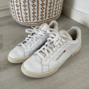 Vita Reebok sneakers i skinn - Klassiska vita Reebok sneakers i skinn med snörning och låg profil. Skorna har rund tå, platt sula och diskret Reebok-logga på sidan och hälen. Perfekta för en clean och stilren look.