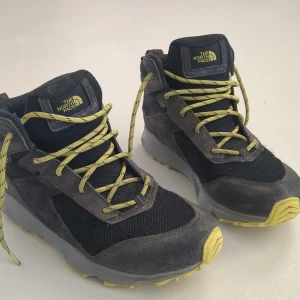 Svarta vandringsskor från The North Face - Svarta vandringsskor/kängor från The North Face med gula snören och grå sula med gula detaljer. Skorna har DryVent-teknologi och är perfekta för utomhusaktiviteter både höst och vinter.