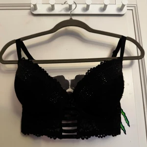 Svart glittrig bh topp med spets - Säljer en svart bh topp med glittriga detaljer och spets. Kuporna är dekorerade med små svarta stenar och har ett snyggt mönster. Nedtill finns flera band och spets 