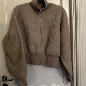 Beige teddyjacka från Bik Bok XL - Mysig beige teddyjacka från Bik Bok i storlek XL. Jackan har hel dragkedja framtill med rund ringdetalj, ribbade muddar och krage.