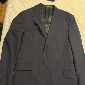 Mörkblå kavaj Oscar Jacobson - Snygg mörkblå kavaj från Oscar Jacobson med klassisk passform och stilrena detaljer. Tillverkad i exklusivt ulltyg från Vitale Barberis Canonico, med slät yta och diskret innerfoder. Perfekt för dig som vill ha en tidlös och elegant look.