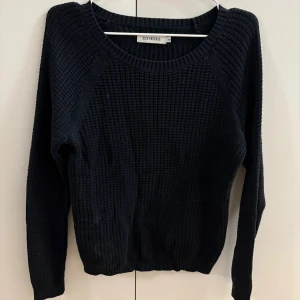 Svart stickad tröja från Size Needle - En svart stickad tröja från Size Needle med grovstickat mönster och rund halsringning. Tröjan har långa ärmar och ribbade muddar vid ärmslut och nederkant. Perfekt för lager-på-lager under kyliga dagar.