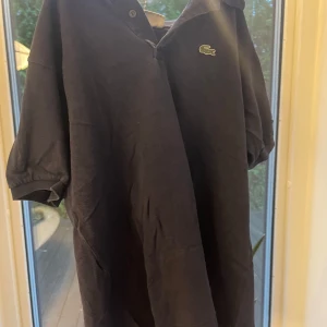 Marinblå pikétröja från Lacoste - Klassisk marinblå pikétröja från Lacoste med den ikoniska gröna krokodilloggan på bröstet. Tröjan har korta ärmar, krage och knäppning framtill. Perfekt för en clean och sportig stil. Tillverkad i bomull för skön känsla.