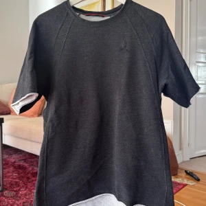 Svart Jordan tjock kortärmad tröja M - Säljer en svart kortärmad tröja från Jordan i storlek M. Tröjan har en enkel och sportig design med diskret broderad logga på bröstet. Tillverkad i mjukt bomullsmaterial som känns skönt mot huden. Perfekt för en avslappnad och cool stil.
