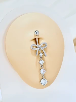 Silverfärgad navelpiercing med rosett - Snygg navelpiercing i silverfärg med en glittrande rosett och hängande stenar. Piercingen har en klassisk stålkula upptill och dekorativa klara stenar som ger extra bling. Perfekt accessoar för dig som vill sticka ut lite extra.