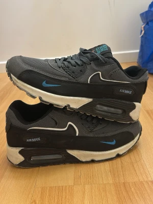 Nike Air Max Sun Club svarta sneakers - Svarta Nike Air Max Sun Club sneakers med blå detaljer och vit sula. Ovandel i mesh och syntet med klassisk Air Max-dämpning. Snyggt broderad logga på plösen och blå swoosh på sidan. Perfekta för dig som gillar streetstyle och sportig look.