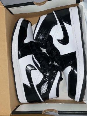 Nike Air Jordan 1 svartvita sneakers - Snygga Nike Air Jordan 1 sneakers i svart och vitt med glansiga detaljer. Klassisk design med svart swoosh, snörning och rund tå. Perfekta för dig som vill sticka ut med en ikonisk och stilren look. Helt oanvända i kartong.