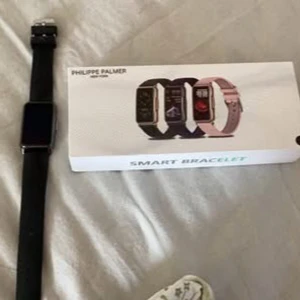 Svart smartklocka från Philippe Palmer - Snygg svart smartklocka från Philippe Palmer med rektangulär urtavla och svart armband. Perfekt för den teknikintresserade som vill hålla koll på sin hälsa och aktivitet. Kommer i originalförpackning. Katt finns i hemmet 