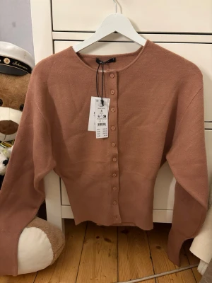 kofta från Ginatricot med knappar - Supersöt kofta från Ginatricot med rund halsringning och knäppning framtill. Koftan är ribbstickad i mjukt material och har långa ärmar. Perfekt att slänga över en topp eller klänning för en chill look.