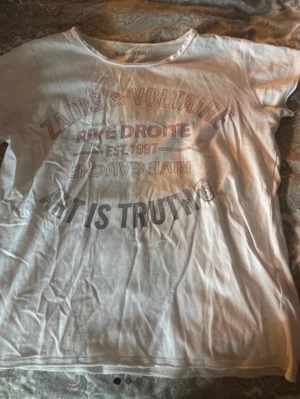 Vit t-shirt från Zadig & Voltaire - Vit t-shirt från Zadig & Voltaire med tryck i flera färger framtill. Rund halsringning och avslappnad passform. Snyggt statement-tryck med texten 'ART IS TRUTH' och andra grafiska detaljer. Perfekt för en cool och avslappnad stil.
