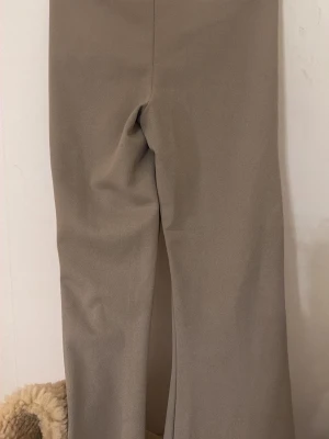 Beige kostymbyxor med bootcut - Stilrena beige kostymbyxor med bootcut-silhuett. Byxorna har en klassisk passform och är tillverkade i ett mjukt material som ger en dressad look. Perfekta för dig som gillar en tidlös och clean stil.