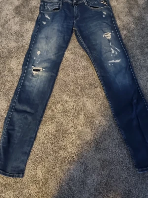 Blå Replay Anbass jeans  - Säljer ett par blå Replay Anbass jeans med snygga detaljer. Jeansen har klassisk femficksmodell och smal passform som sitter riktigt bra. Perfekta för dig som gillar en trendig och avslappnad stil.storlek 30 k midjan 32 i längd