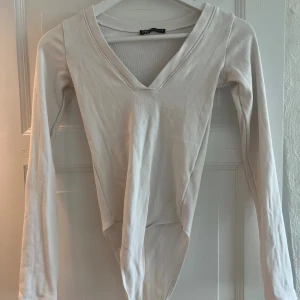 Vit långärmad body med V-ringning - Säljer en stilren vit body från zara med lång ärm och djup V-ringning. Bodyn har en enkel och clean design, perfekt att matcha med olika outfits. Tillverkad i mjukt stretchigt material för en bekväm passform. Ett perfekt basplagg!