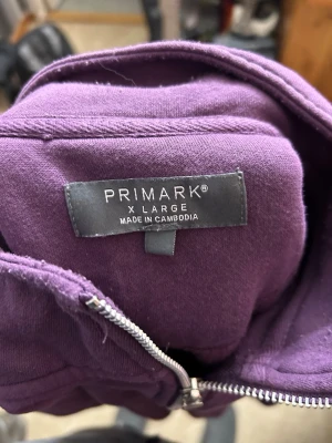 Lila hoodie med dragkedja från Primark - Säljer en lila hoodie från Primark i storlek XL. Hoodien har en halv dragkedja framtill och är gjord i mjukt bomullsmaterial. Perfekt för dig som gillar en enkel och stilren look med en poppig färg. Långa ärmar och ribbade muddar vid ärmslut och nederkant.