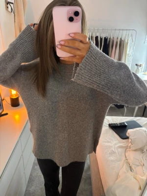 Grå oversized stickad tröja - Mysig grå stickad tröja med oversized passform och långa ärmar. Tröjan har ribbade muddar vid ärmslut och nederkant samt slitsar på sidorna för en avslappnad look🩶